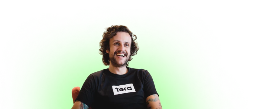 Foto de um homem sorrindo. Ele está vestindo uma camiseta preta com o logo da Tera no centro.